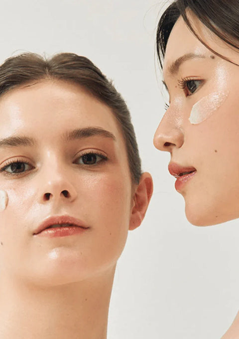 To kvinder med glødende hud og påført creme fra en Koreansk hudplejeserie i minimalistisk lys opsætning.