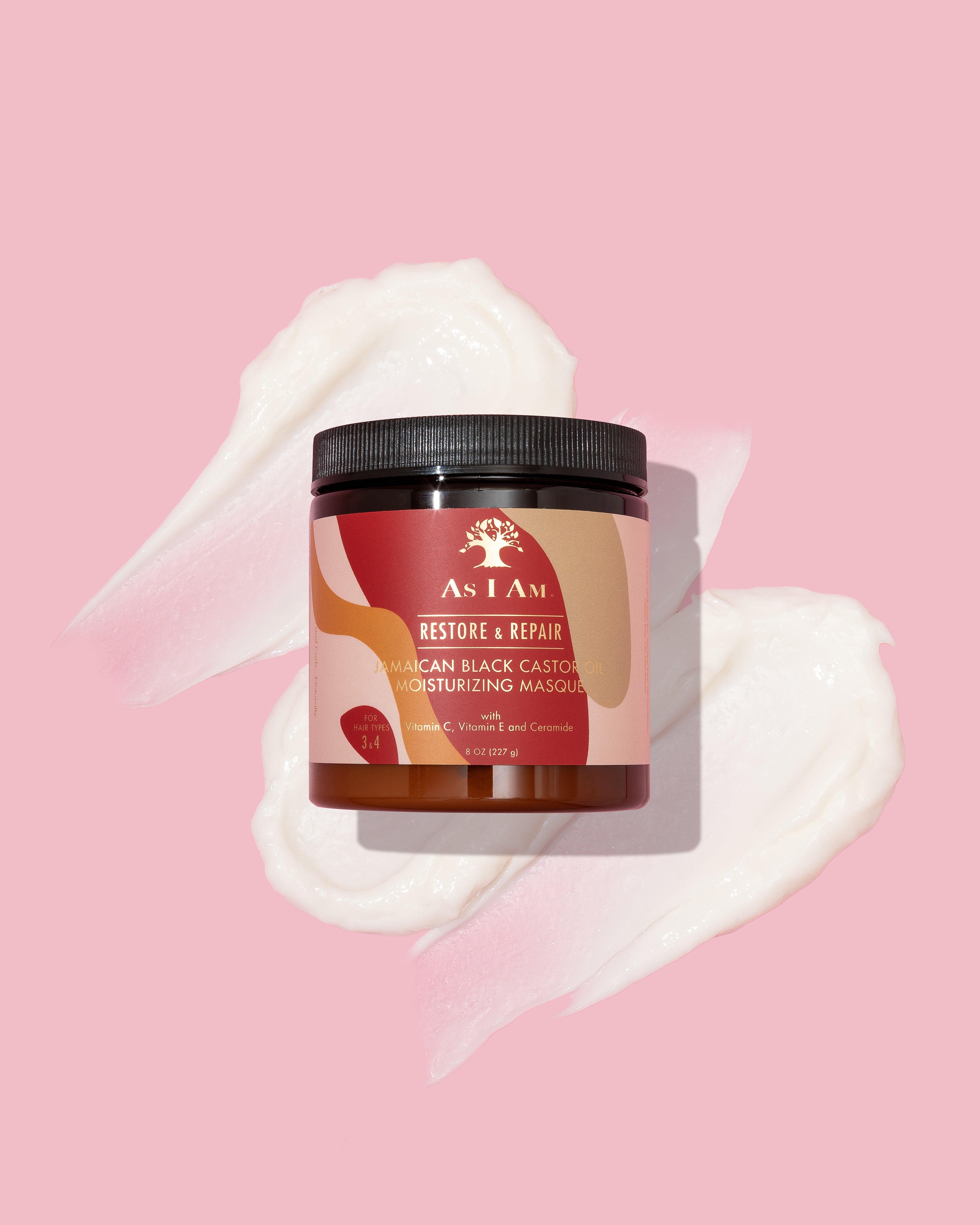 As I Am Jamaican Black Castor Oil Moisturizing Masque (227 g) placeret på en lyserød baggrund med tre hvide, cremede klatter af masken spredt omkring.