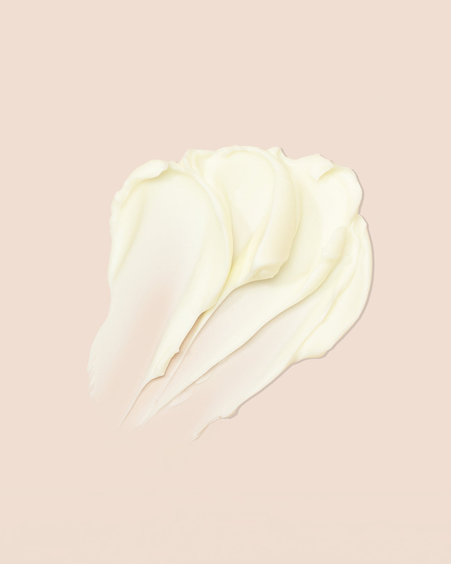 Et tæt billede af en klump hvid creme på en lyserød baggrund. Cremen er smurt ud i bløde, bølgede streger. Billedet viser indeholdet af produktet As I Am Classic DoubleButter Cream.