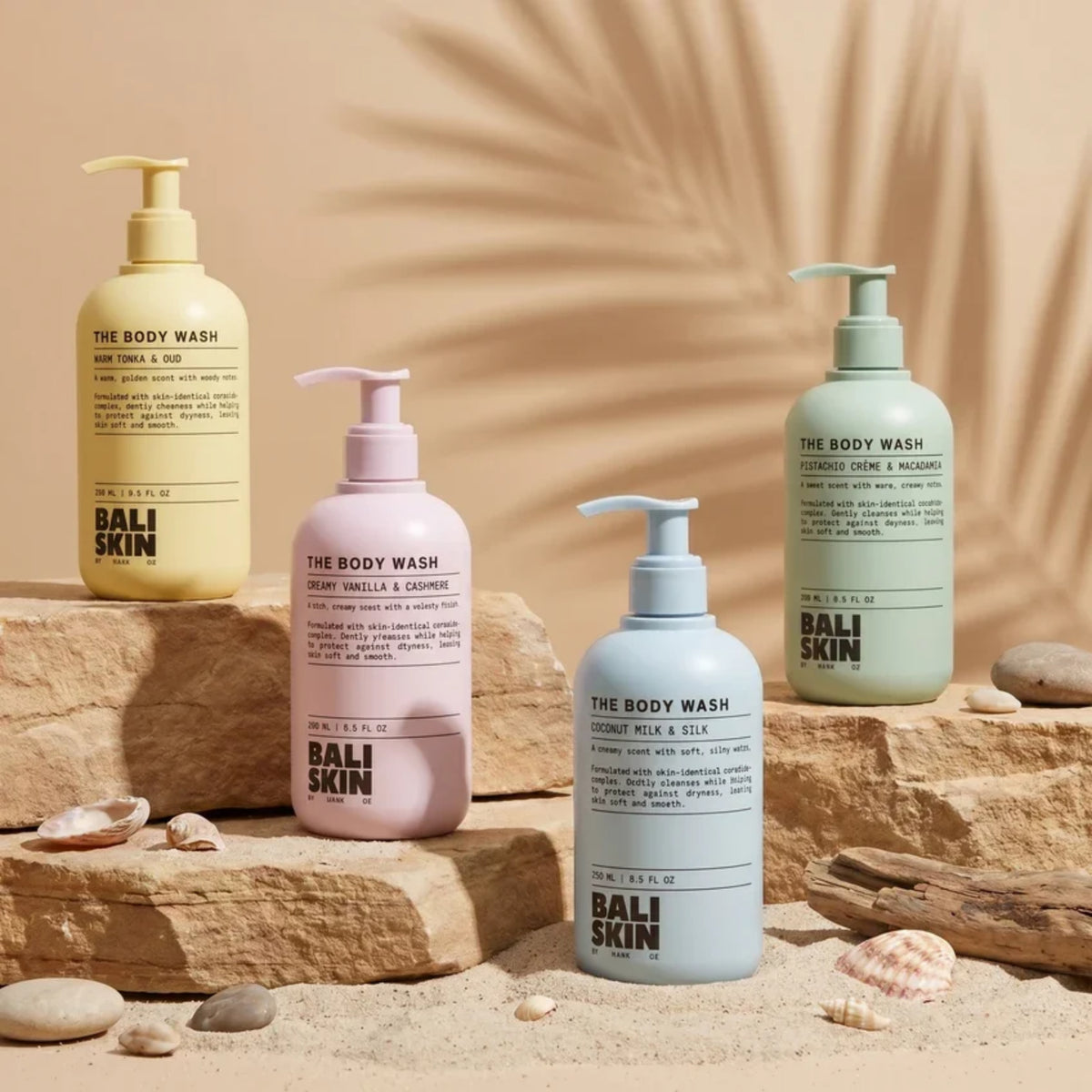 Fire Bali Skin bodywash-flasker i gul, lyserød, blå og grøn på sten og sand med skaller.