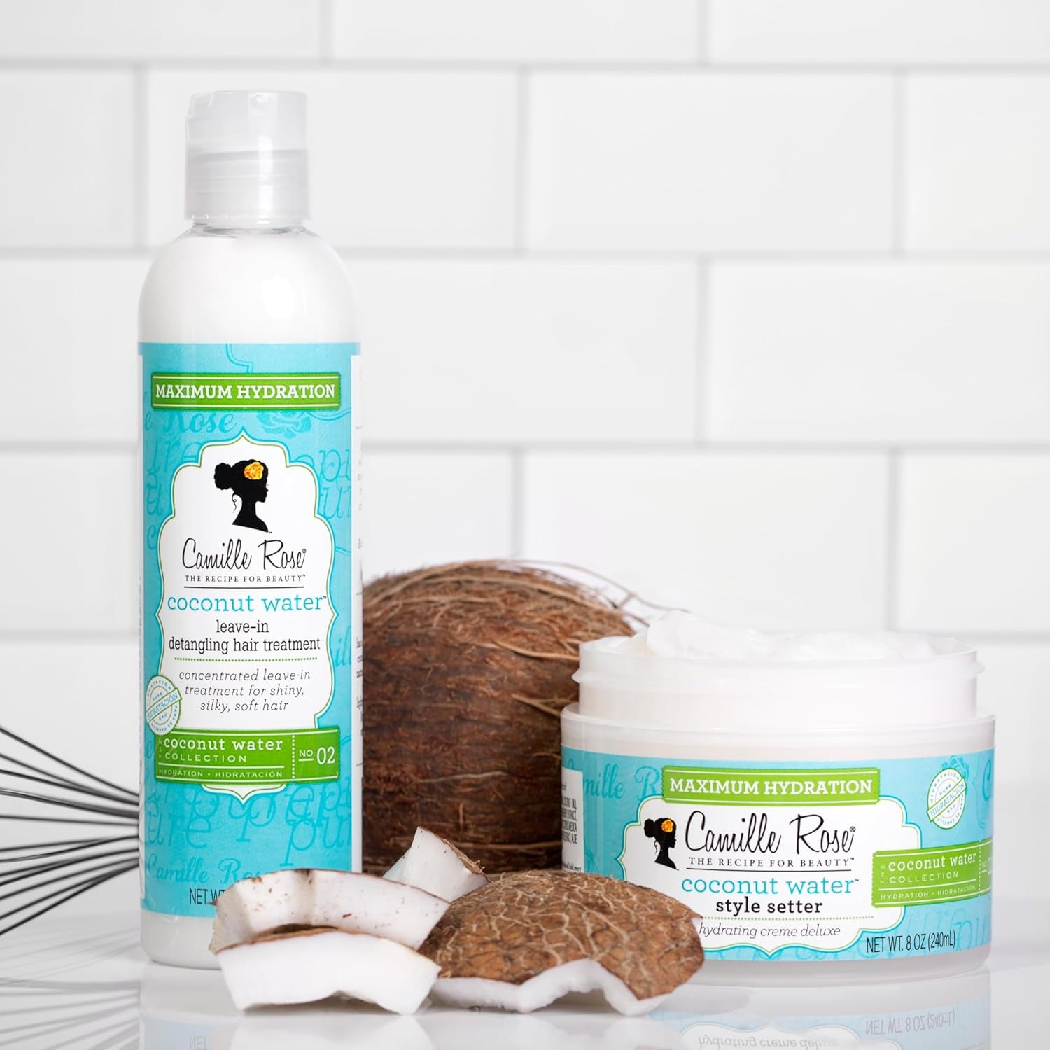 Hvid flaske med Camille Rose Coconut Water Leave-In Treatment og krukke med Style Setter ved siden af en hel og stykker af en kokosnød.
