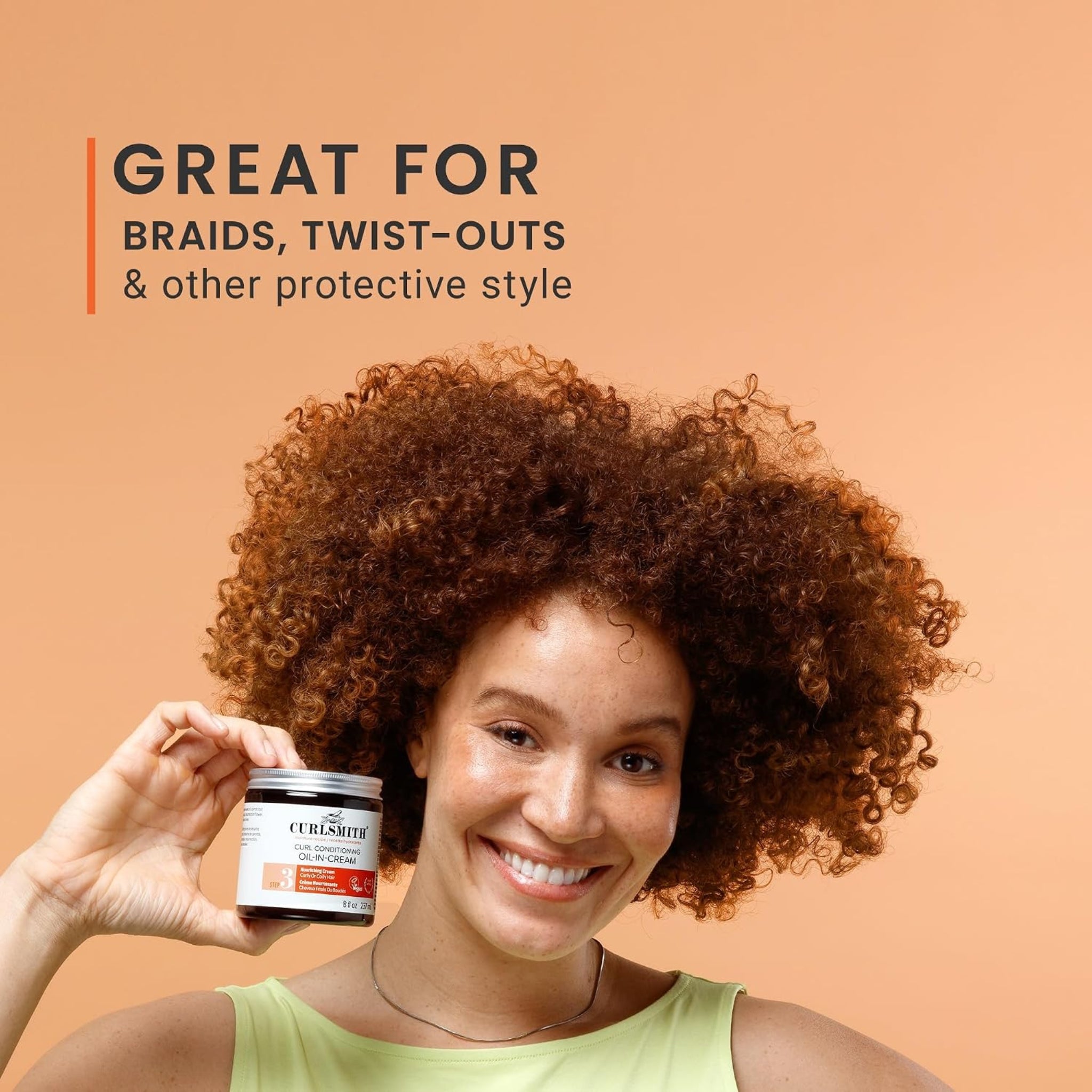 Kvinde med krøllet rødbrunt hår smiler og holder Curlsmith Curl Conditioning Oil-In-Cream, ideel til fletninger og twist-outs.