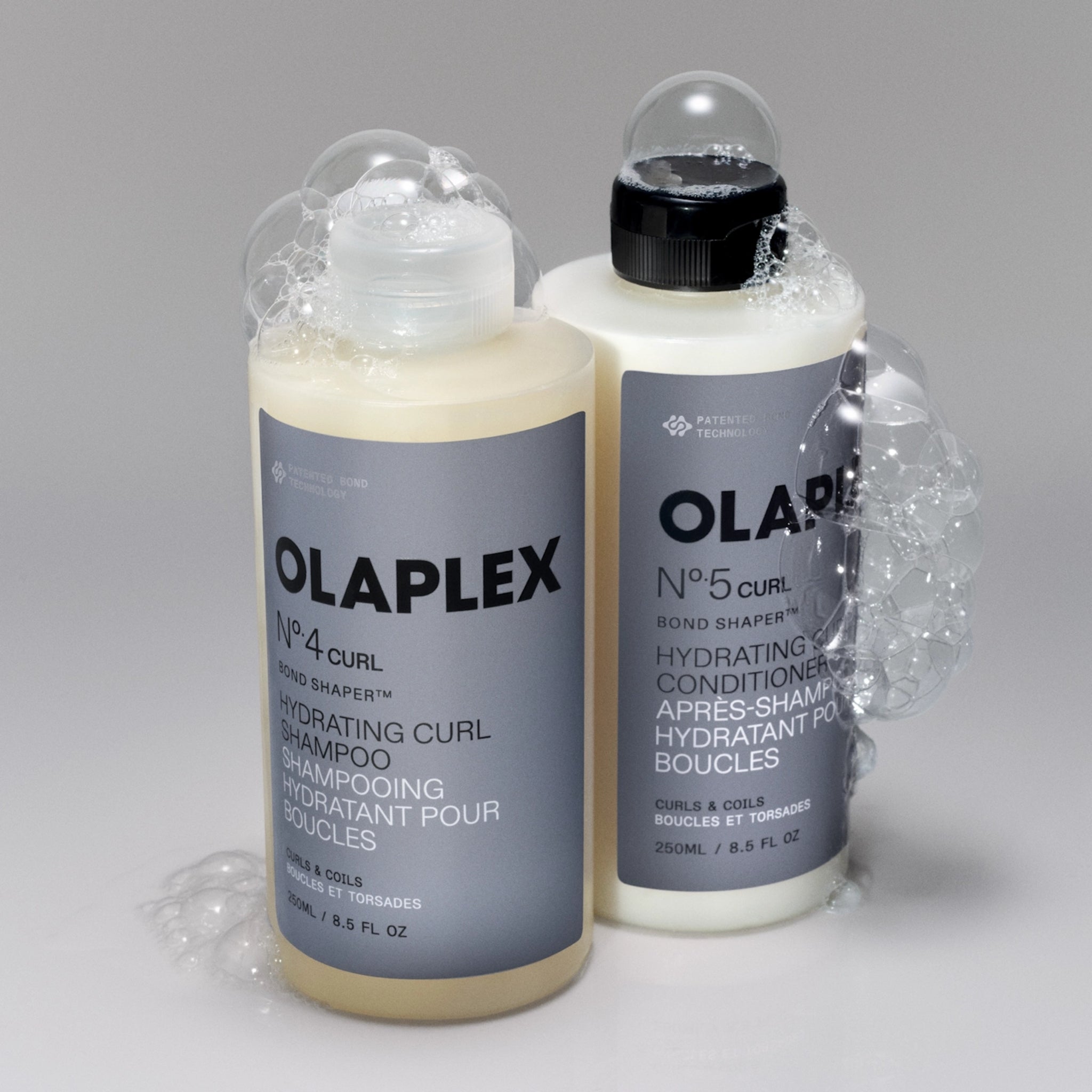 Olaplex No.4 Curl shampoo og No.5 Curl conditioner med skum på grå baggrund.