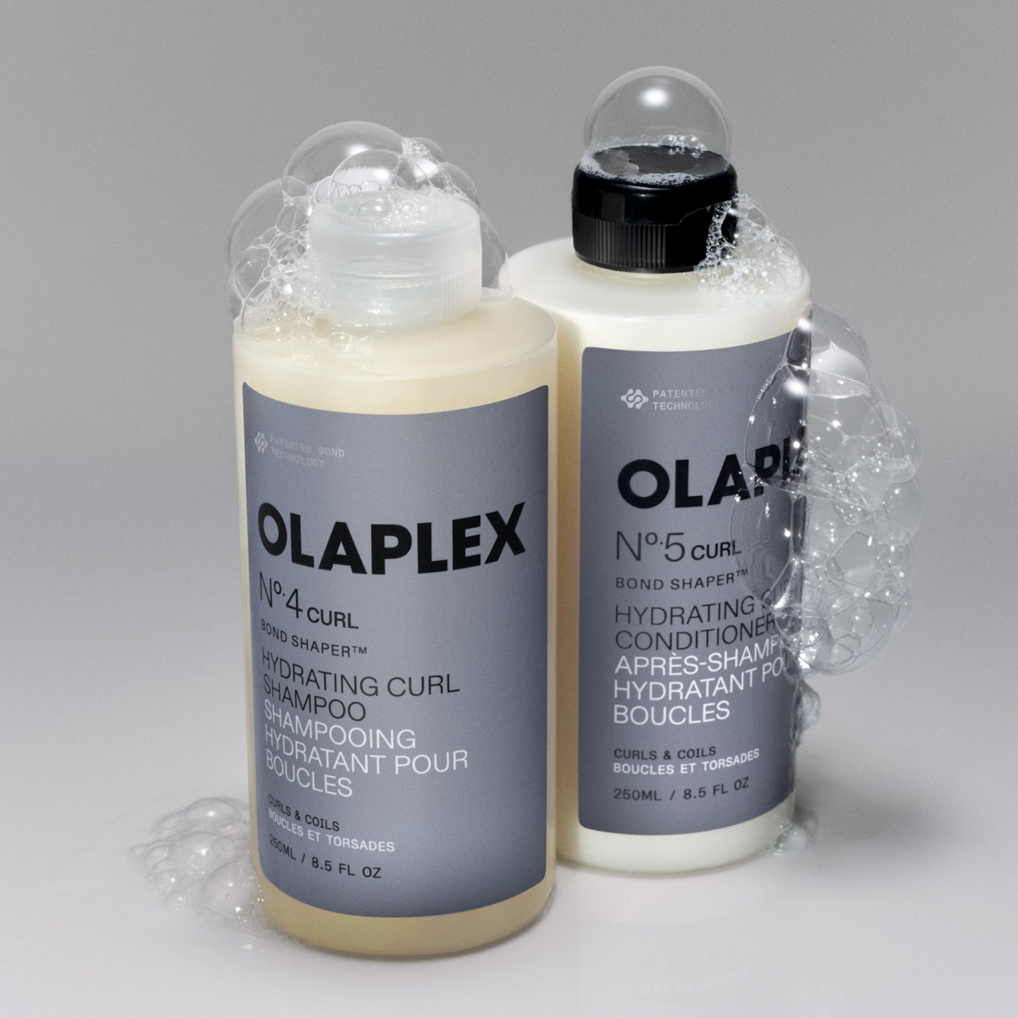 Olaplex No. 4 Curl shampoo og No. 5 Curl conditioner med skum mod grå baggrund.