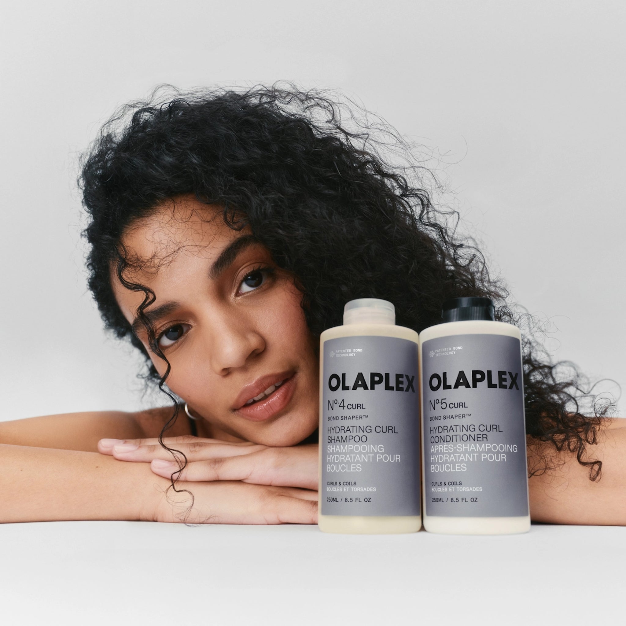 Kvinde med krøllet hår ved siden af Olaplex No.4 Curl shampoo og No.5 Curl conditioner til krøller.