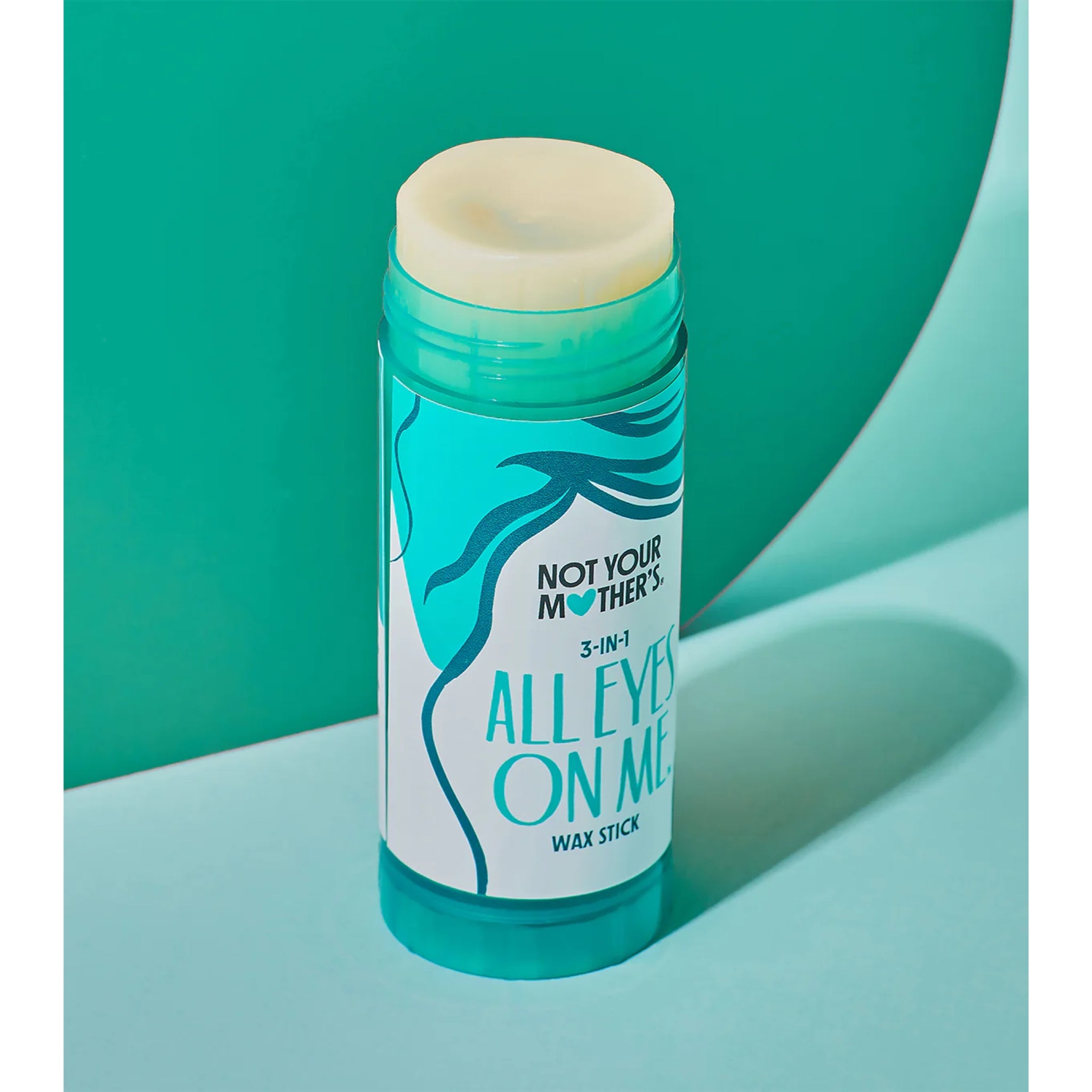 Not Your Mother's All Eyes On Me 3-in-1 wax stick i turkis tube på grøn baggrund.
