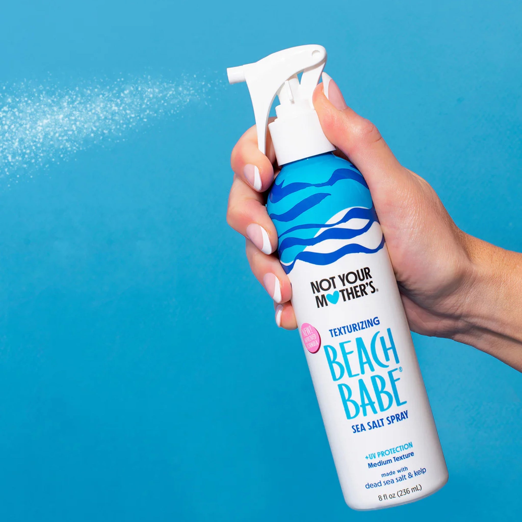 Hånd sprøjter Not Your Mother's Beach Babe sea salt spray mod blå baggrund.