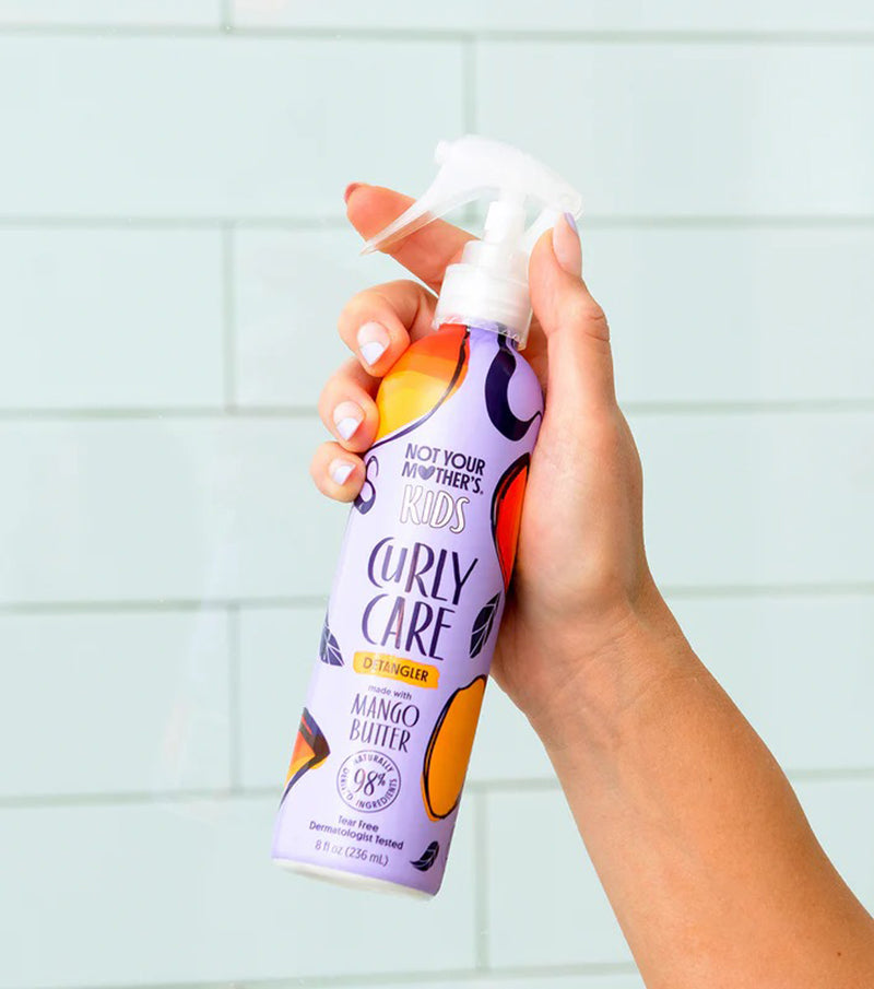 Hånd holder Not Your Mother's Kids Curly Care Detangler 236ml med farverig emballage foran lyse fliser.