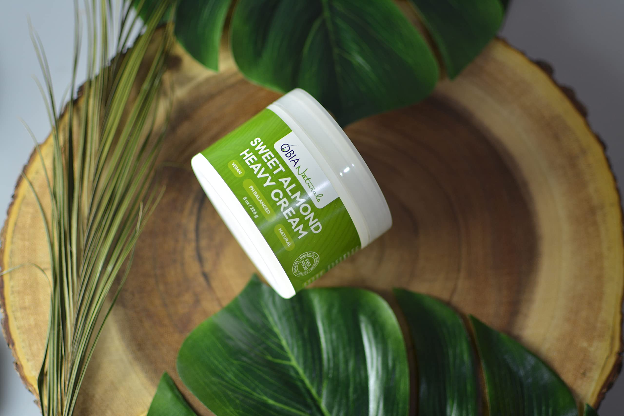 OBIA Naturals Sweet Almond Heavy Cream (226g) præsenteret med grønne blade på en træskive.