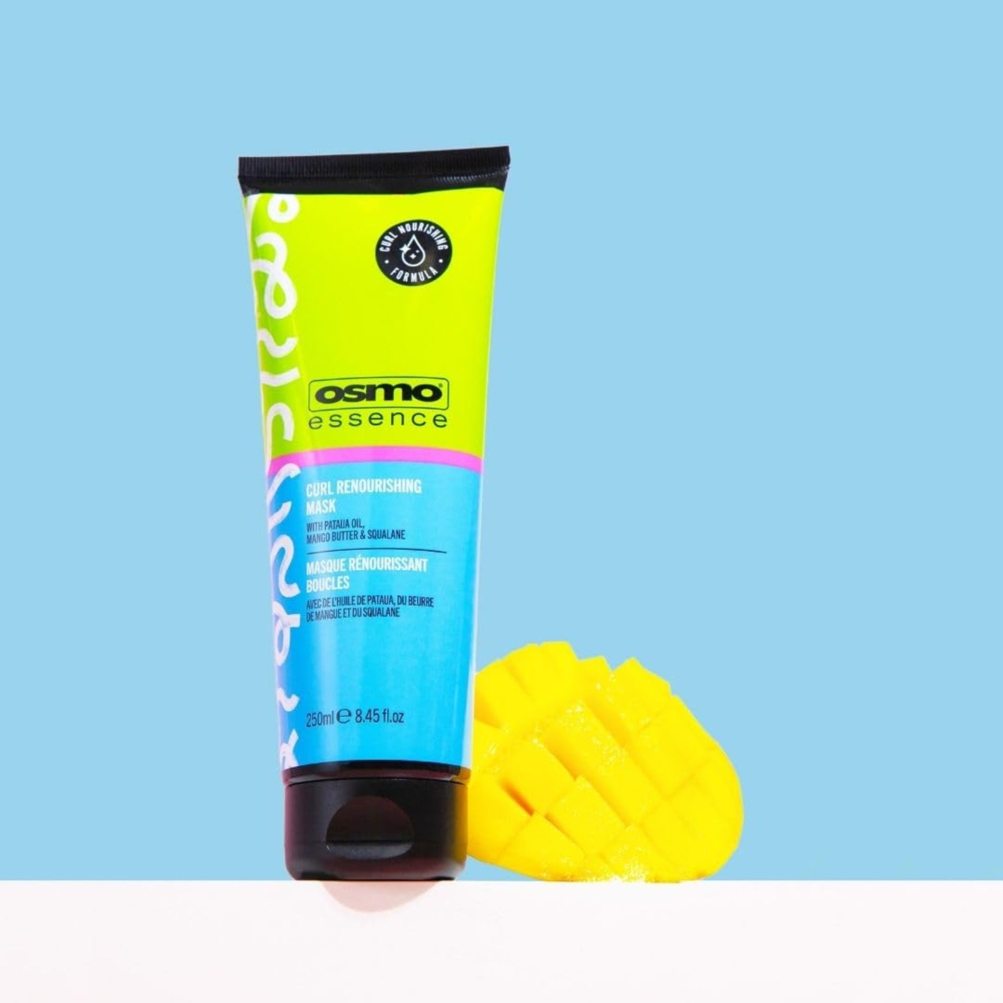 Osmo Essence Curl Renourishing Mask tube på 250 ml med en udskåret mango ved siden af på lyseblå baggrund.