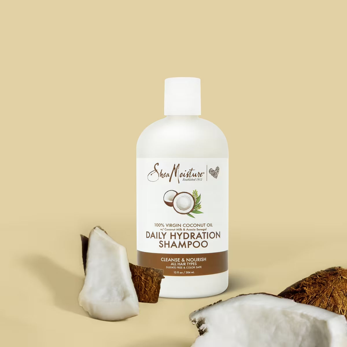 Produktet er Shea Moisture 100% Virgin Coconut Oil Daily Hydration Shampoo, 384ml. Shampooen er sulfatfri og farvebeskyttende, og den er velegnet til alle hårtyper. Flasken står foran en beige baggrund med kokosnødder.