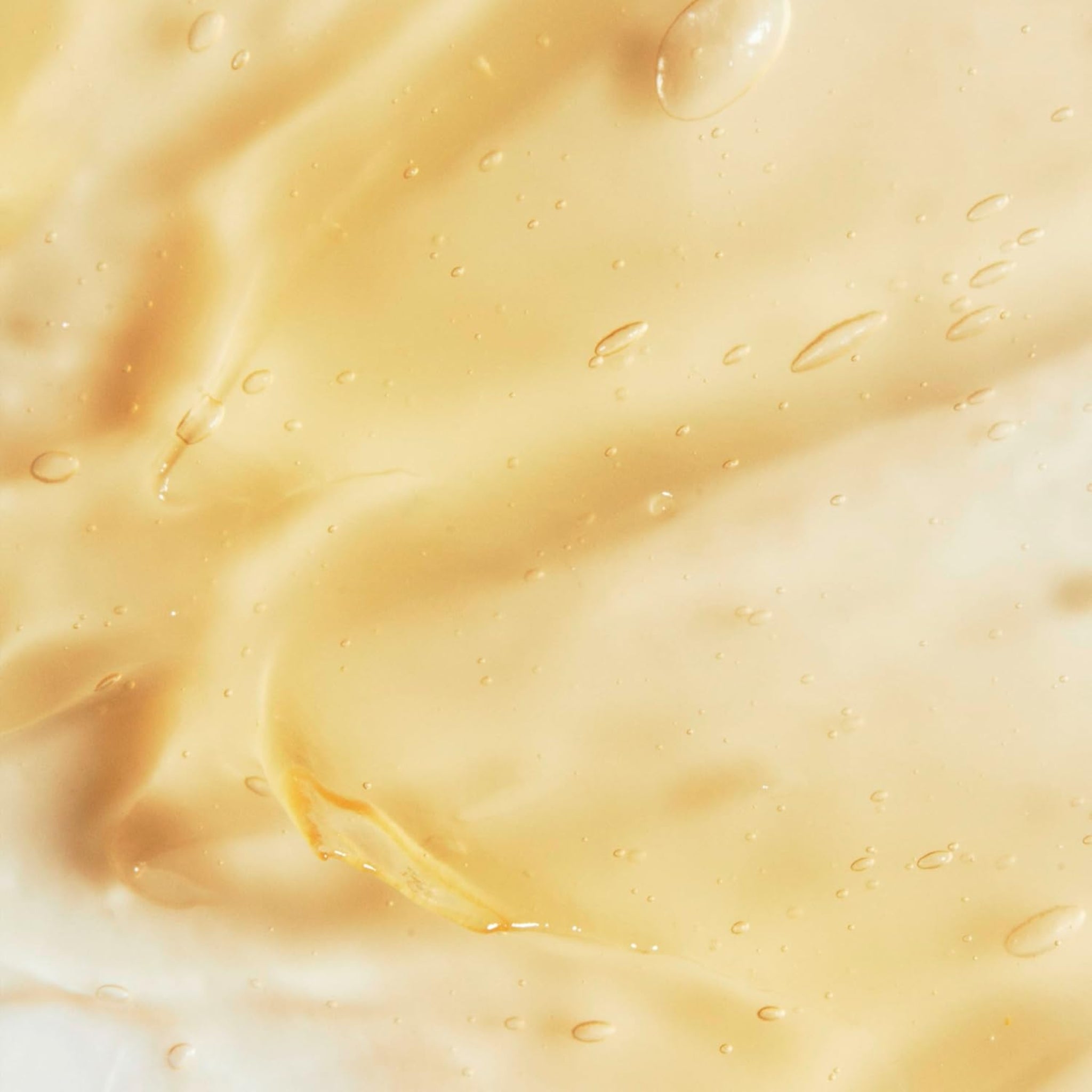 Gyldent, gelélignende hudplejeprodukt i nærbillede med bobler og bølgede teksturer i cremefarvet og gyldent nuance.